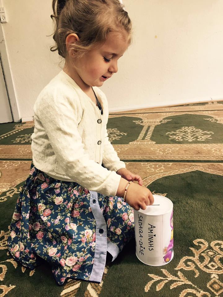 Lille pige putter penge i en dåse i moske